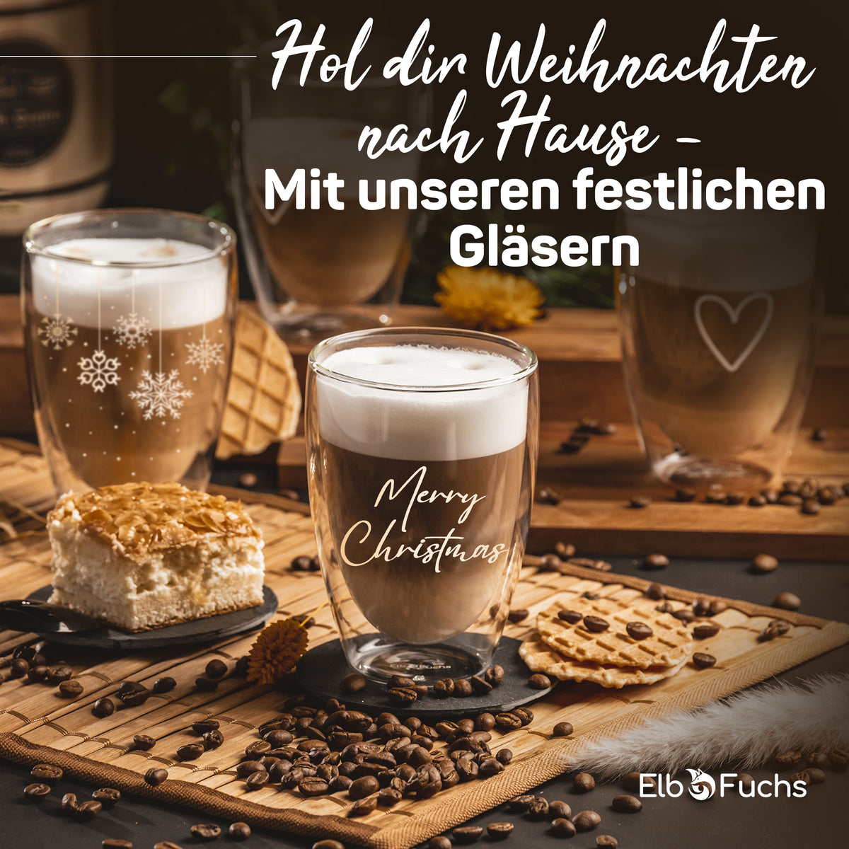Weihnachtliche Tischszene mit ElbFuchs Thermogläsern gefüllt mit Latte macchiato, umgeben von Kaffeebohnen, Gebäck und einer Torte, im Hintergrund ein weiteres Glas mit herzförmiger Gravur.