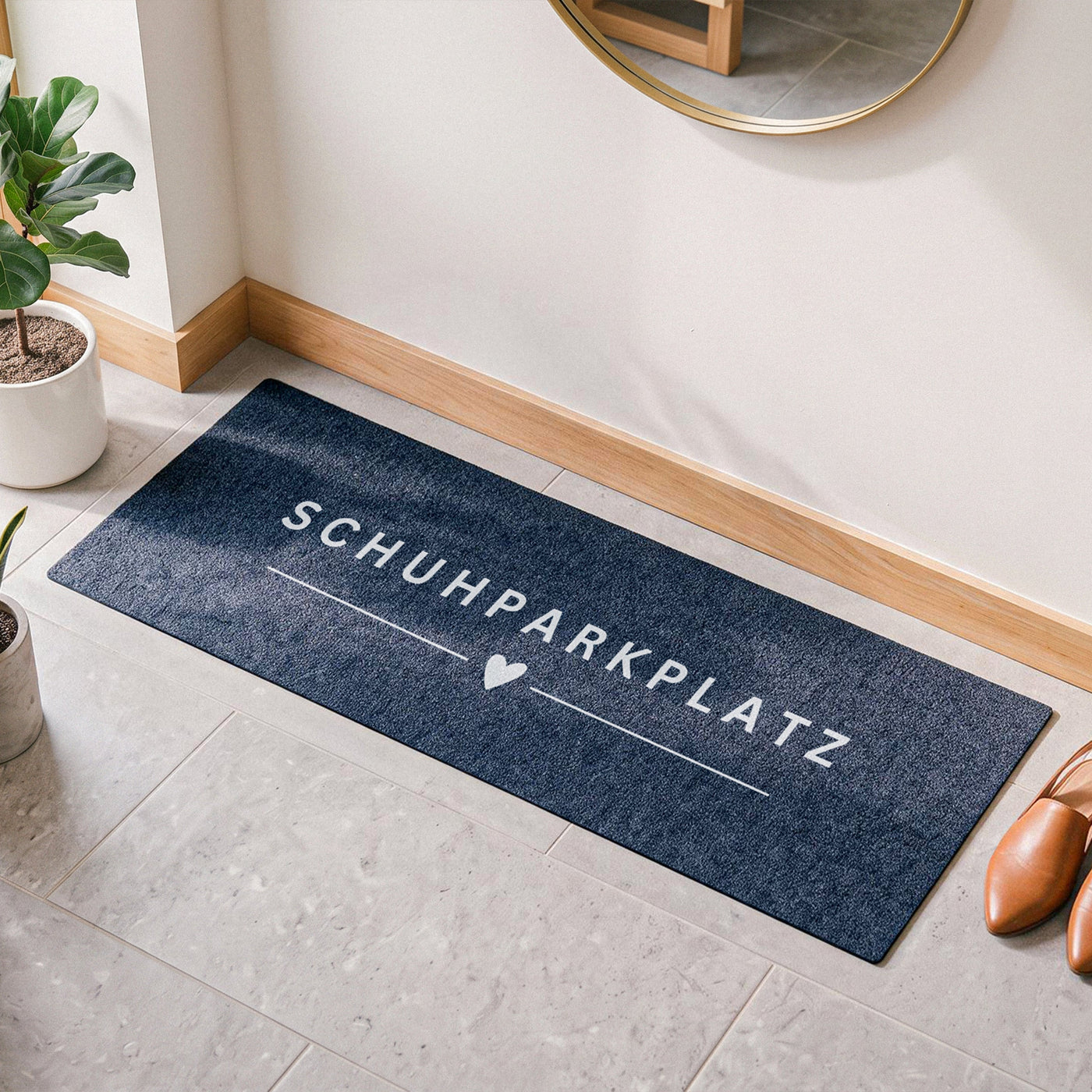 Schmale anthrazite Fußmatte mit weißem Aufdruck „SCHUHPARKPLATZ“ und Herz-Motiv (100x35 cm), platziert auf hellen Fliesen im skandinavisch eingerichteten Flur neben braunen Schuhen und Zimmerpflanzen.