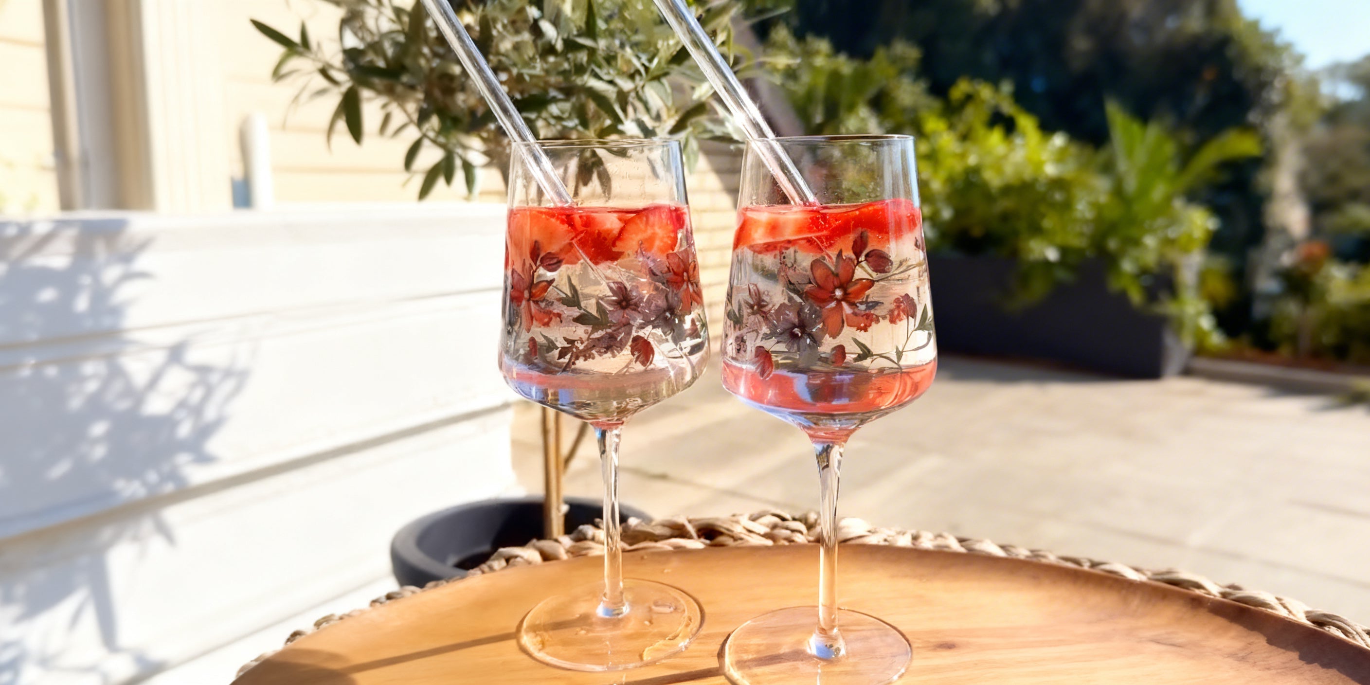 Set aus zwei ElbFuchs Aperitifgläsern mit floralem Blumen-Design und nachhaltigen Glasstrohhalmen. Serviert mit Erdbeeren und Eis auf einem Holztablett in der Hamburger Abendsonne.