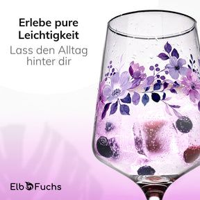 Nahaufnahme eines ElbFuchs Glases 'Violet Veil' mit violettem Blütenmotiv, gefüllt mit einem hellen Getränk, Eiswürfeln und dunklen Beeren, vor sanft lila changierendem Hintergrund.