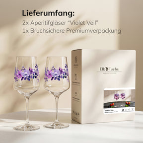 ElbFuchs Geschenkset 'Violet Veil': zwei mit violetten Blüten bemalte Weingläser stehen auf einem hellen Tisch neben der Verpackung im warmen Streiflicht.