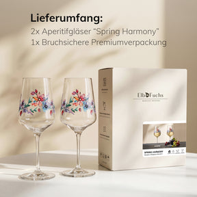 ElbFuchs Geschenkset 'Spring Harmony': zwei blumenverzierte Weingläser stehen vor warmem Lichteinfall neben der Verpackung mit Produktabbildung.