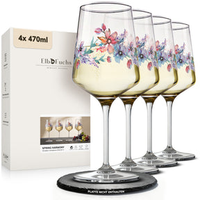 Vier ElbFuchs Weingläser der Serie 'Spring Harmony' mit zartem Blüten-Aquarellmotiv in Rosé- und Lilatönen, gefüllt mit Weißwein und aufgereiht vor der passenden Geschenkverpackung.