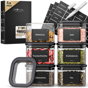 Sechs ElbFuchs BLACK KONTOR Vorratsgläser à 400 ml mit schwarzem Deckel, gefüllt mit Walnüssen, Salz, Trockenfrüchten, Kürbiskernen, Chiasamen und Tee, inklusive Etiketten und Kreidestift.