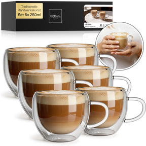 Sechs doppelwandige VIENNA Kaffeegläser mit Henkel, gefüllt mit cremigem Milchkaffee, stehen gestaffelt vor der ElbFuchs Verpackung im Set 6x250ml, daneben ein rundes Detailfoto zweier Hände, die eines der Gläser wärmend umschließen.