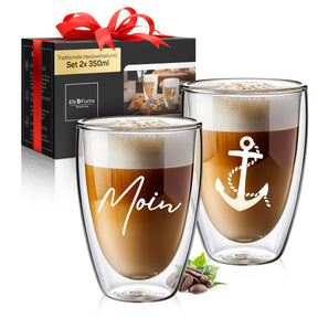 ElbFuchs Geschenkset aus zwei doppelwandigen 350-ml-Gläsern mit der Gravur 'Moin' und einem maritimen Anker-Motiv, gefüllt mit Latte macchiato, daneben die passende schwarze Geschenkbox mit roter Schleife vor weißem Hintergrund.