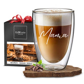 Ein ElbFuchs Doppelwandiges Glas 350ml mit der Gravur 'Mama', gefüllt mit cremigem Latte Macchiato, steht vor einer schwarzen Geschenkbox mit roter Schleife und ElbFuchs Logo.