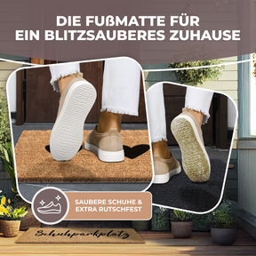 Nahaufnahme zweier Schuhsohlen, die über eine ElbFuchs Kokos-Fußmatte mit Herz-Motiv streifen, mit dem Hinweis 'Saubere Schuhe & extra rutschfest'. Im Hintergrund ist verschwommen ein Hauseingang mit einer weiteren beschrifteten Fußmatte 'Schuhparkplatz' zu erkennen.