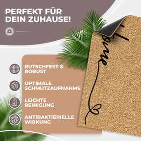 Die hochgeklappte ElbFuchs Kokosfußmatte „Home“ zeigt ihre schwarze rutschfeste Unterseite vor Palmblättern, begleitet von Hinweisen zu Robustheit, Schmutzaufnahme, leichter Reinigung und antibakterieller Wirkung.
