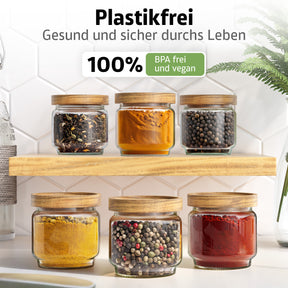Sechs ElbFuchs Gewürzgläser mit Olivenholzdeckel stehen auf einem hellen Holzregal vor einer weißen Fliesenwand, gefüllt mit getrockneten Kräutern, Kurkuma, Pfefferkörnern, Currypulver, Pfeffermischung und Paprikapulver; der Hinweis betont die plastikfreie, BPA-freie und vegane Ausführung.