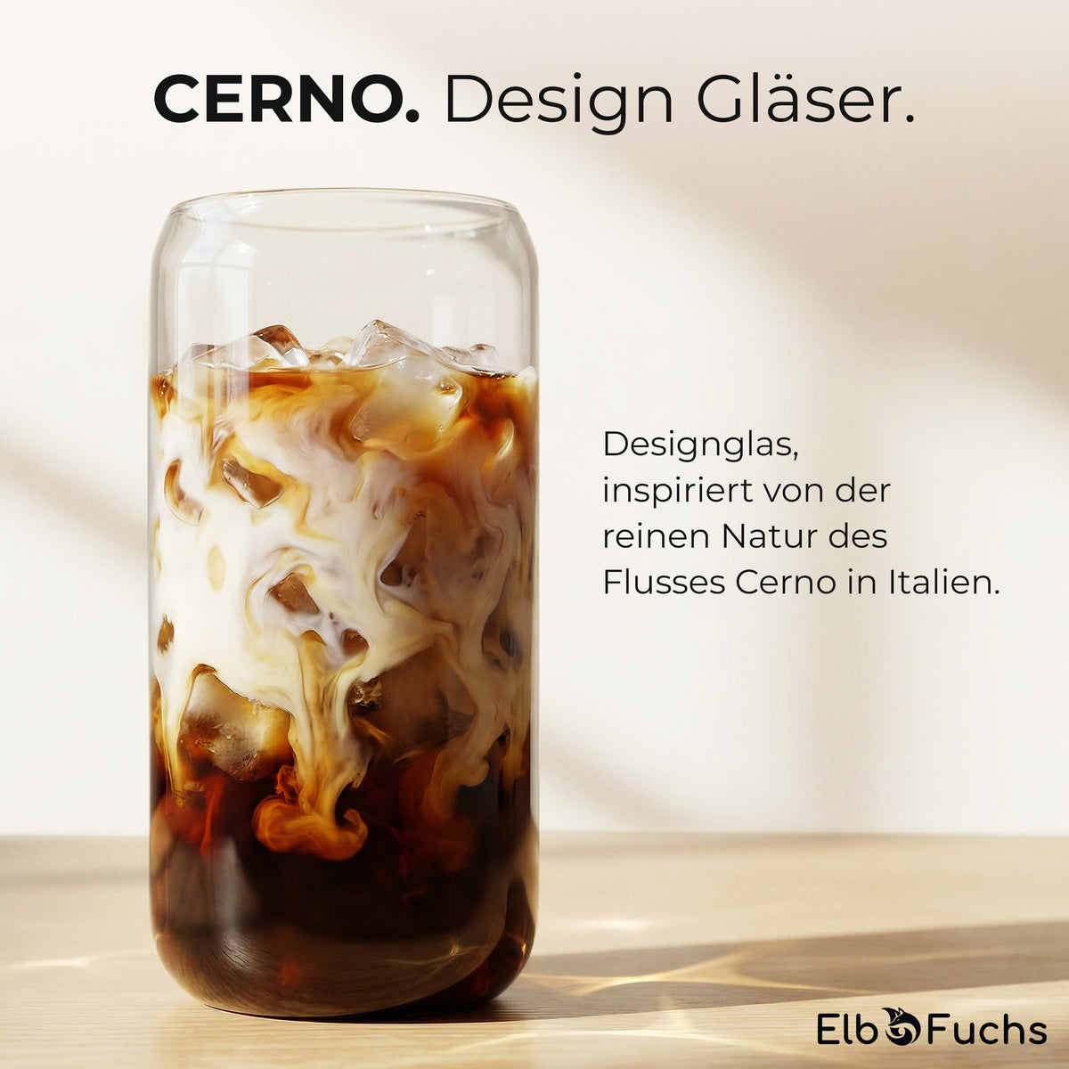 Ein ElbFuchs CERNO Designglas mit cremigem Iced Coffee und Eiswürfeln auf einem sonnenbeschienenen Holztisch, der Text verweist auf die Inspiration durch den Fluss Cerno in Italien.
