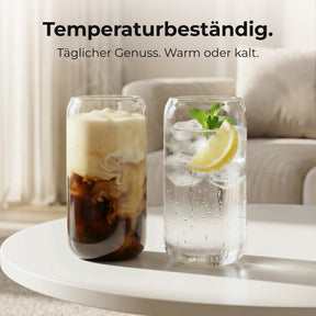 Zwei ElbFuchs CERNO Gläser auf einem runden Couchtisch im Wohnzimmer, eines gefüllt mit cremigem Iced Coffee, das andere mit spritzigem Wasser, Eiswürfeln, Minze und einer Zitronenscheibe, dazu der Hinweis auf die Temperaturbeständigkeit der Gläser.