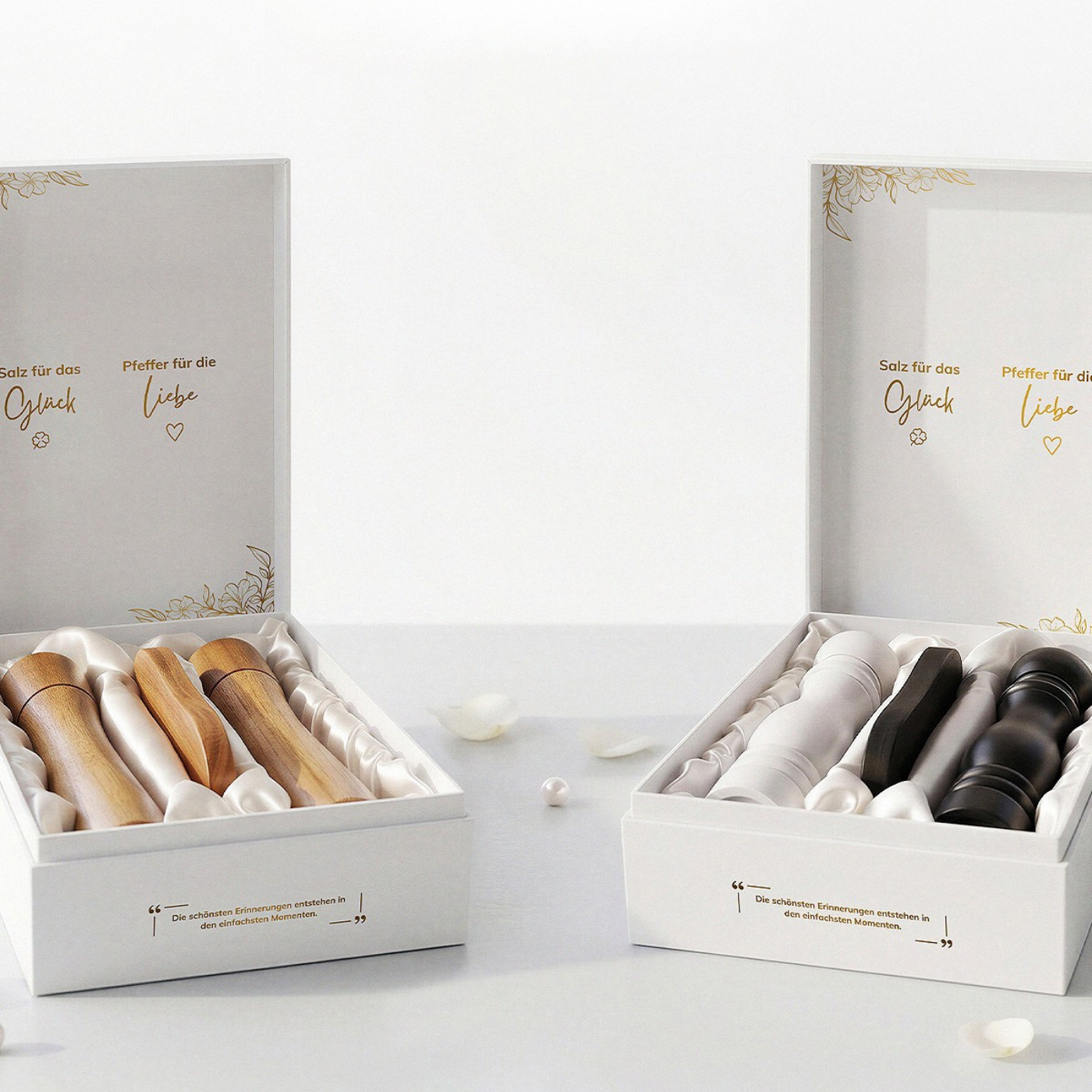 Zwei geöffnete, elegante weiße ElbFuchs Geschenkkartons präsentieren jeweils ein dreiteiliges Salz- und Pfeffermühlen-Set, gebettet auf edlem, weißem Satinstoff. Das linke Set besteht aus natürlichem Holz mit passendem Holzuntersetzer; das rechte Set kombiniert eine weiße und eine schwarze Mühle mit dunkler Menage. Die Deckelinnenseiten sind mit den Schriftzügen 'Salz für das Glück' und 'Pfeffer für die Liebe' verziert, während die Vorderseite der Boxen den gravierten Spruch.