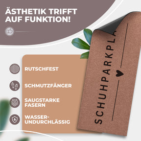 Eine aufgerollte mokkabraune ElbFuchs Schuhparkplatz Fußmatte mit vertikalem Schriftzug und Herz-Symbol sowie sichtbarer schwarzer, rutschfester Unterseite vor grünen Blättern; Icons zeigen Rutschfestigkeit, Schmutzfang und Wasserundurchlässigkeit.