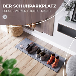 Der graue ElbFuchs Schuhparkplatz mit der Aufschrift 'Schuhparkplatz' und rosa Herzen liegt im Eingangsbereich unter einem hölzernen Schuhschrank, darauf stehen ordentlich drei Paar Schuhe – braune Schnürschuhe, graue Sneaker und orangefarbene Stiefeletten – neben einem geflochtenen Korb auf hellem Holzboden.