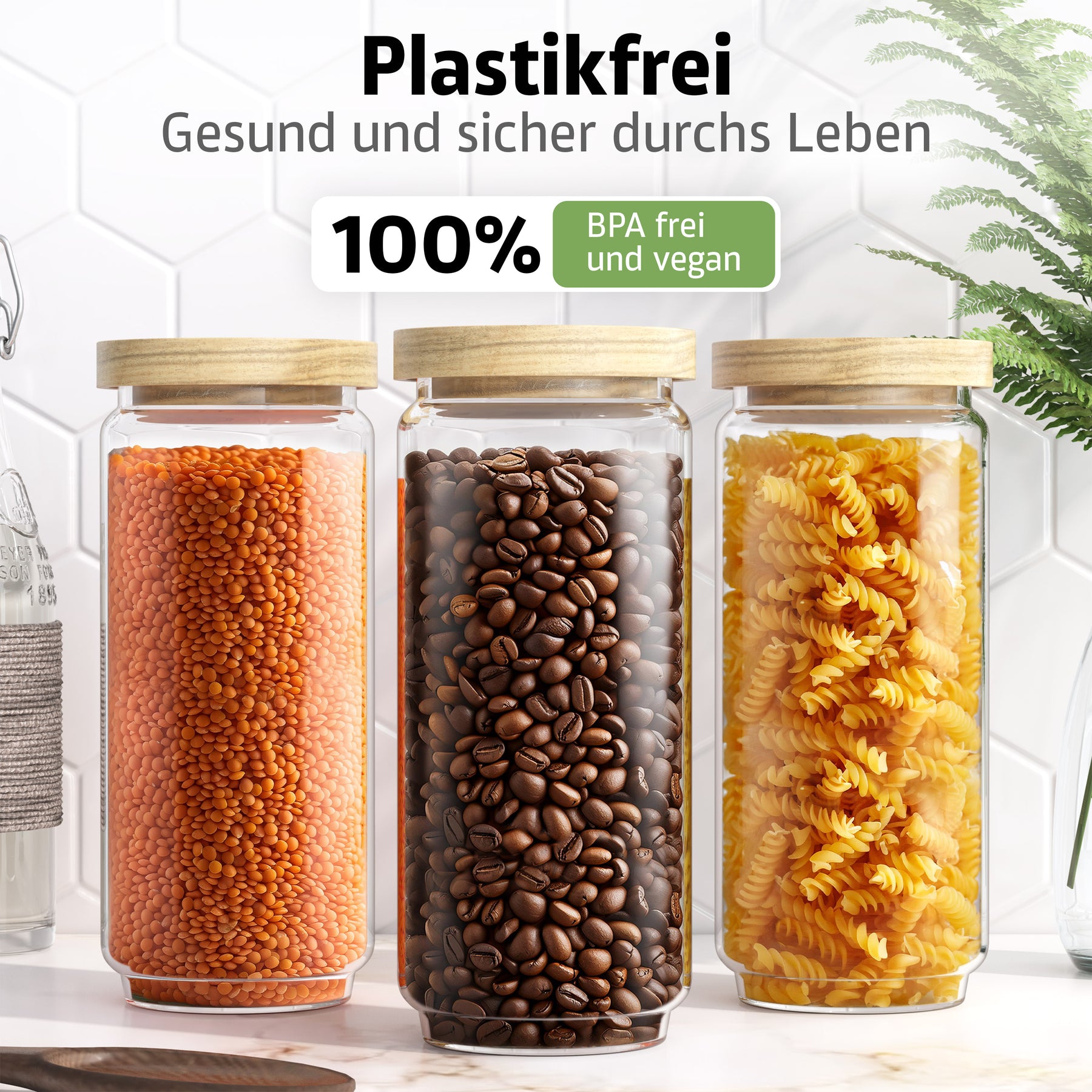 Drei ElbFuchs Vorratsgläser WOOD KONTOR mit Holzdeckeln stehen nebeneinander auf einer Marmorplatte, gefüllt mit roten Linsen, Kaffeebohnen und gelben Fusilli, vor weißen Hexagonfliesen mit grüner Pflanze.