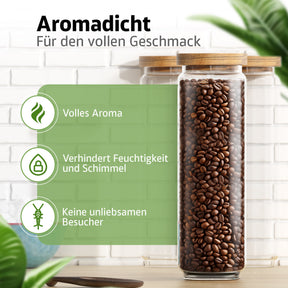 Ein schlankes, hohes ElbFuchs Vorratsglas mit Bambusdeckel ist bis zum Rand mit dunklen Kaffeebohnen gefüllt und steht vor einer weißen Ziegelwand mit grünen Blättern im Hintergrund.