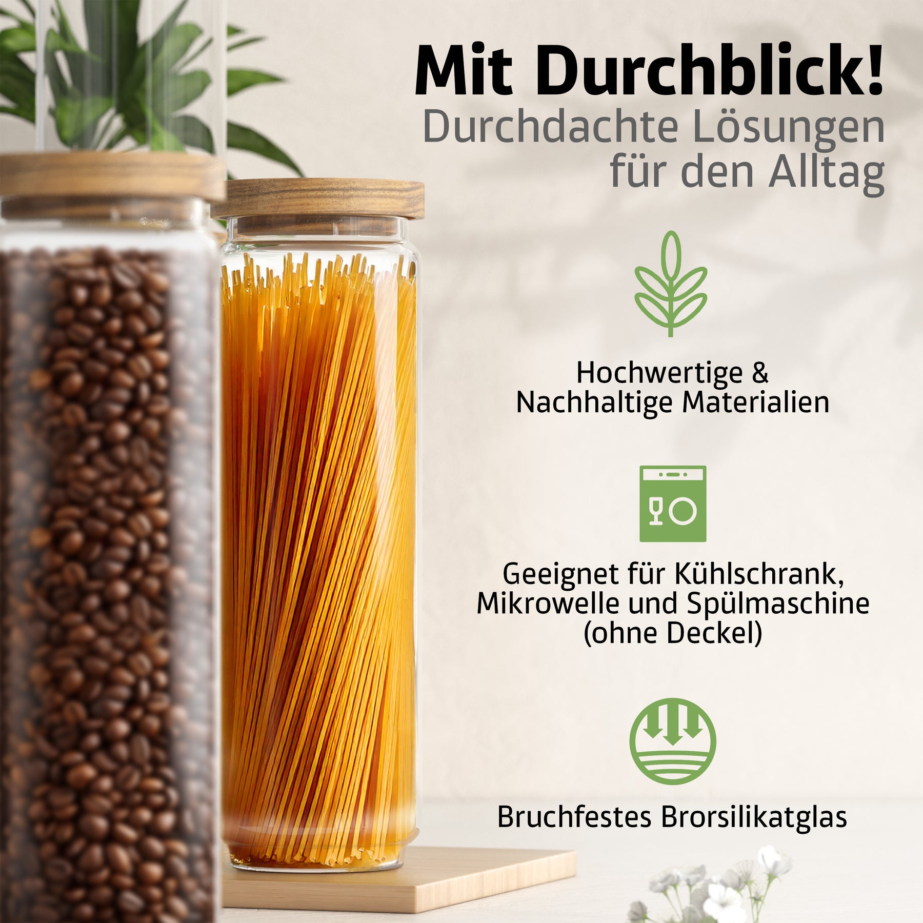 Zwei ElbFuchs Vorratsgläser mit Bambusdeckel und bruchfestem Borosilikatglas stehen auf einem hellen Holzbrett, das eine mit Kaffeebohnen, das andere mit aufrecht stehenden Spaghetti gefüllt, umrahmt von grünen Blättern und kleinen weißen Blüten.
