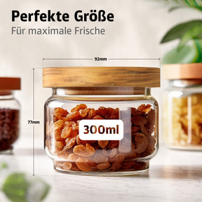 Ein ElbFuchs Vorratsglas WOOD KONTOR mit Holzdeckel und goldenen Rosinen gefüllt zeigt die Maße 92 mm Durchmesser und 77 mm Höhe bei 300 ml Volumen, umgeben von weiteren Gläsern mit dunklem Gewürz und Walnüssen.