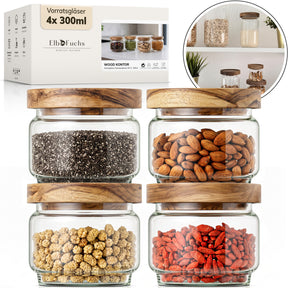 Die ElbFuchs Verpackung der Vorratsgläser 4x 300ml Serie WOOD KONTOR steht neben vier quadratischen Gläsern mit Deckeln aus Olivenholz, gefüllt mit Chiasamen, Mandeln, getrockneten Maulbeeren und Gojibeeren; ein runder Bildausschnitt zeigt die Gläser griffbereit im Küchenregal.