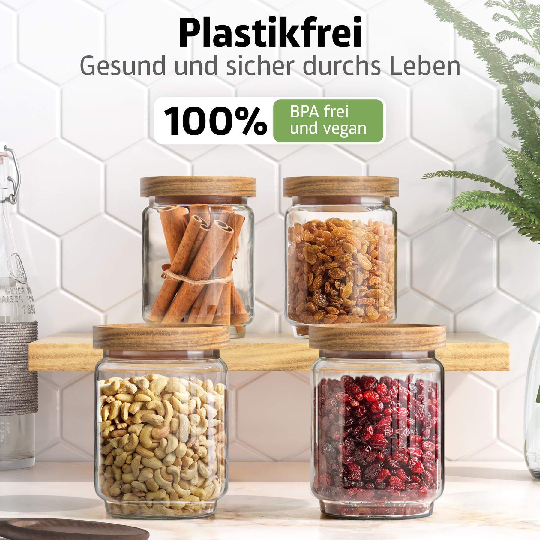 Vier ElbFuchs Vorratsgläser WOOD KONTOR mit Holzdeckeln stehen auf einem Holzbrett, gefüllt mit Zimtstangen, goldenen Rosinen, Cashewkernen und getrockneten Cranberries, vor weißen Hexagonfliesen mit grüner Pflanze.