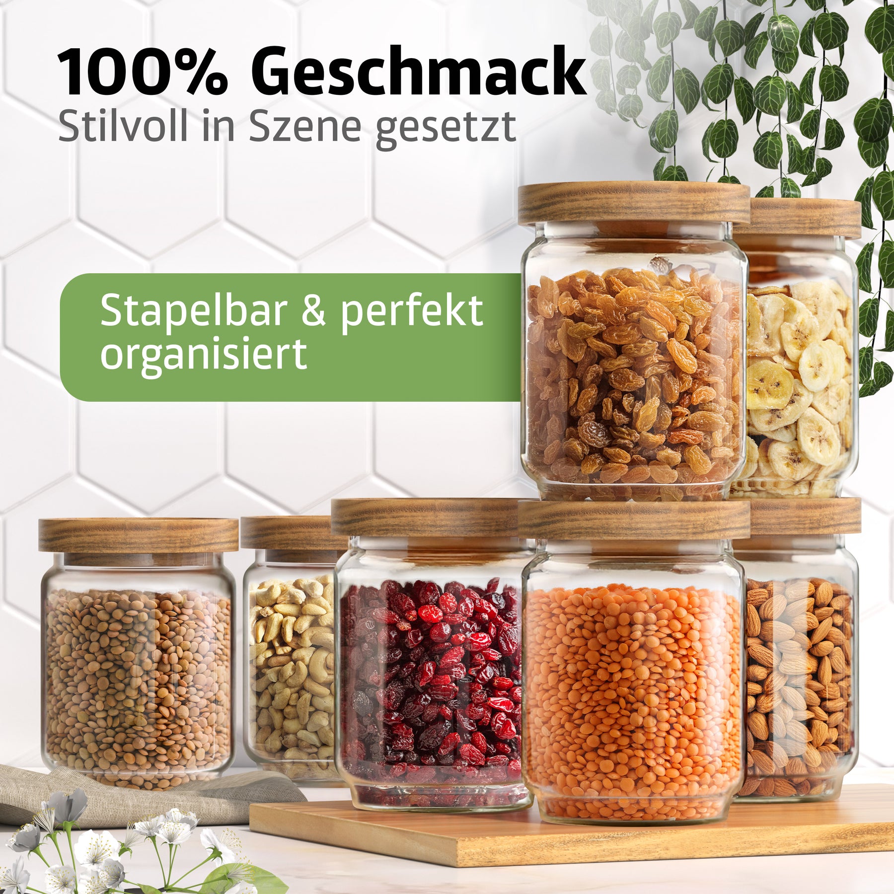 Sieben ElbFuchs Vorratsgläser WOOD KONTOR mit Holzdeckeln sind pyramidenförmig gestapelt und mit Rosinen, Bananenchips, braunen Linsen, Cashewkernen, getrockneten Cranberries, roten Linsen und Mandeln gefüllt, vor einer weißen Fliesenwand mit hängenden Ranken.