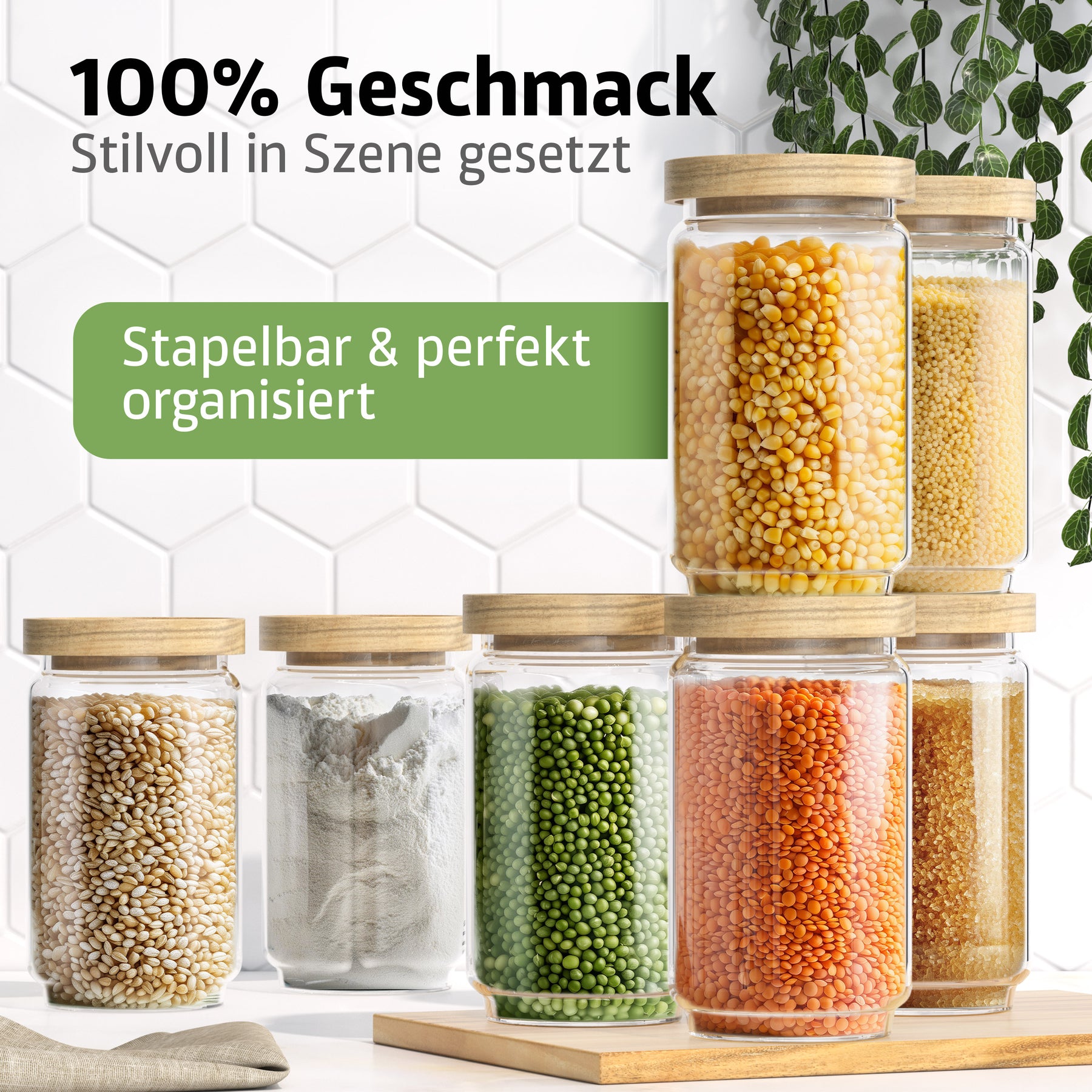 Sieben ElbFuchs Vorratsgläser WOOD KONTOR mit Holzdeckeln sind pyramidenförmig gestapelt und mit Mais, Hirse, Popcornmais, Mehl, grünen Erbsen, roten Linsen und braunem Zucker gefüllt, vor einer weißen Fliesenwand mit hängenden Ranken.