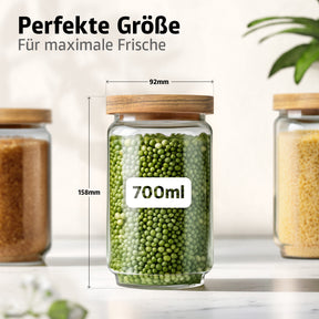 Ein ElbFuchs Vorratsglas WOOD KONTOR mit Holzdeckel und grünen Erbsen gefüllt zeigt die Maße 92 mm Durchmesser und 158 mm Höhe bei 700 ml Volumen, umgeben von weiteren Gläsern mit braunem Zucker und Hirse.