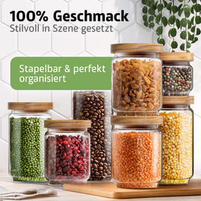 Mehrere unterschiedlich große ElbFuchs Vorratsgläser mit Holzdeckel sind stapelbar angeordnet und mit Rosinen, buntem Pfeffer, grünen Erbsen, getrockneten Cranberries, Kaffeebohnen, Linsen und Mungbohnen befüllt, vor einer weißen Fliesenwand mit hängender Grünpflanze.