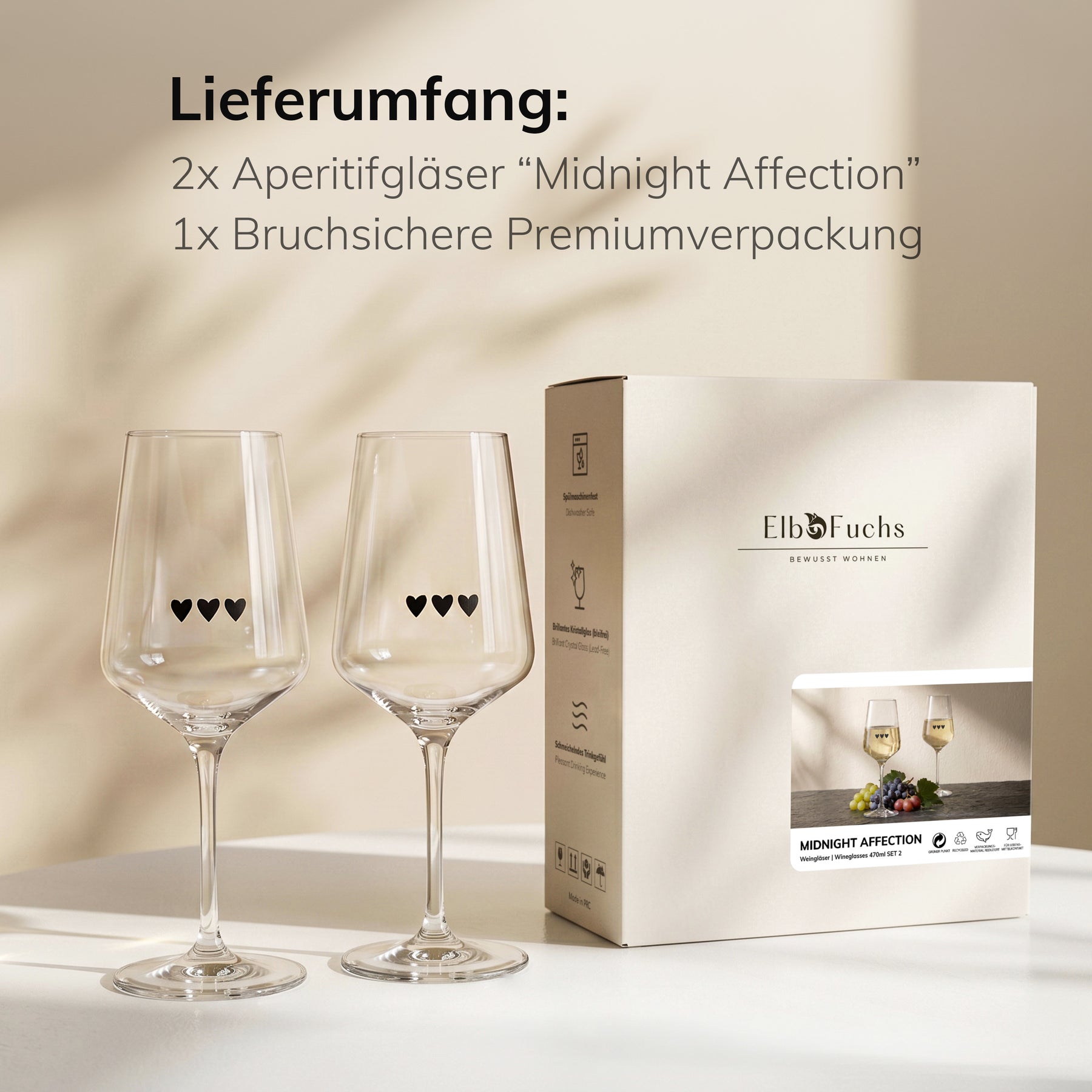 ElbFuchs Geschenkset 'Midnight Affection': zwei Weingläser mit feiner Herzgravur stehen auf einem hellen Tisch neben der Verpackung im warmen Streiflicht.