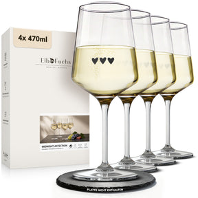 Vier ElbFuchs Weingläser 'Midnight Affection' mit dezenter Herzgravur, gefüllt mit hellem Weißwein, aufgereiht vor der passenden Geschenkverpackung auf einer Schieferplatte.